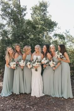 a group of women standing next to each other holding bouquets in front of trees