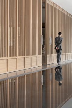 a man in a suit standing next to a wall with wooden slats on it