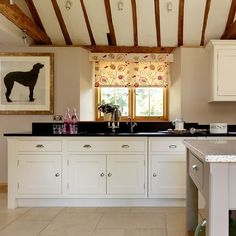 a kitchen with white cabinets and black counter tops in front of a painting on the wall