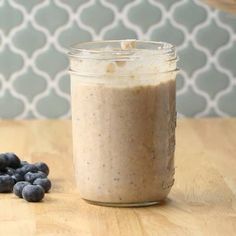 a jar filled with blueberries sitting on top of a wooden table next to a spoon