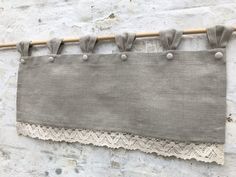 an old curtain hanging on a clothes line with buttons and lace around the edges, in front of a white brick wall