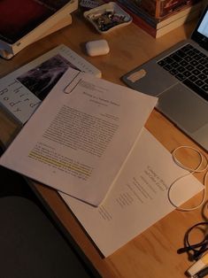 an open laptop computer sitting on top of a wooden desk next to papers and headphones