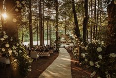 an outdoor ceremony in the woods with white flowers and greenery on either side of the aisle