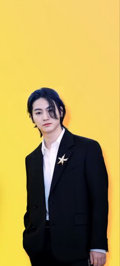 a man in a black suit and white shirt posing for a photo against a yellow background