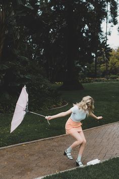 a woman is playing with an umbrella on the sidewalk in front of some grass and trees