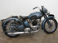 a blue motorcycle parked in a room next to a white wall and cement flooring