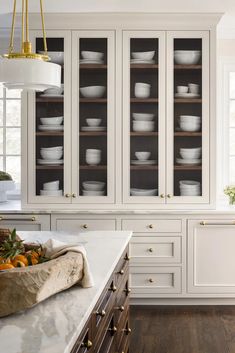 a kitchen with white cabinets and marble counter tops, gold pulls on the glass doors