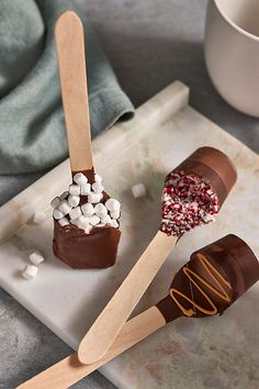 two chocolate covered marshmallows on wooden spoons