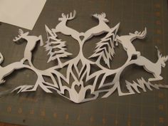 paper cut out of deers and trees on a cutting board with scissors next to it