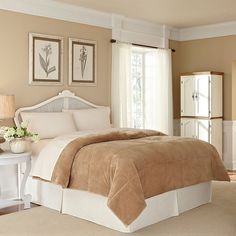 a large bed in a bedroom next to a white table with flowers and two framed pictures on the wall