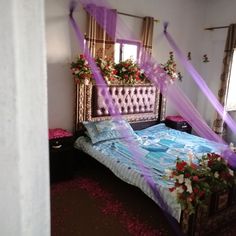 a bed with purple sheer curtains and flowers on the headboard, in a bedroom decorated for valentine's day