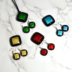 This eye-catching pendant and earrings are made at a small furnace on the island of Murano, Italy, just outside of Venice. Adorned with metallic gold, red, green, or blue, this Italian-made set is the perfect accessory to brighten any outfit. Lamp-worked glass with inset metallic foil submerged under clear glass. Pendant measures approximately 1.3" across. Earrings measure 0.8" across. Made in Murano, Italy Modern Multicolor Rectangular Jewelry, Multicolor Jewelry Making Supplies In Various Shapes, Handmade Glass Square Pendant Jewelry, Handmade Square Glass Pendant Jewelry, Modern Multicolor Jewelry With Unique Variations, Modern Multicolor Glass Jewelry, Multicolor Necklaces With Matching Earrings For Gifts, Handmade Black Jewelry With Square Pendant, Rectangular Multicolor Party Jewelry