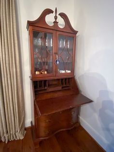 an old wooden china cabinet sitting on top of a hard wood floor next to a window