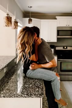 a man and woman sitting on top of a counter in a kitchen next to each other