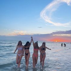 three women in bikinis are standing in the water at the beach with their arms up