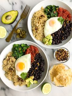 two white bowls filled with rice, beans and an egg next to avocado