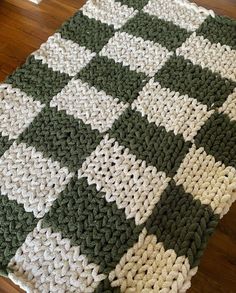 a green and white crocheted blanket sitting on top of a hard wood floor