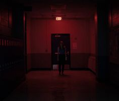 a woman standing in a dark hallway with red lights on the ceiling and walls behind her