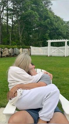 two people are sitting on a bench in the grass and one person is wrapped up