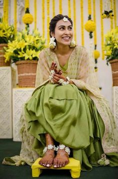 a woman sitting on top of a yellow bench wearing a green dress and flower garlands