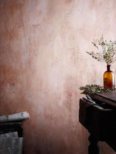 a vase with some flowers on top of a wooden table next to a brown wall