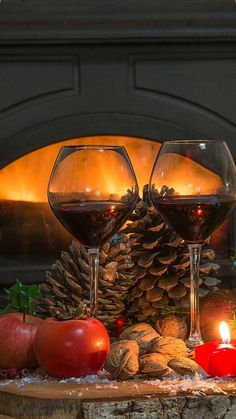 two glasses of wine sitting on a table next to an open fire place with fruit and candles