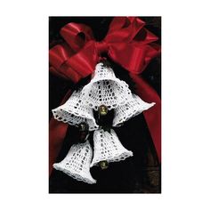 three white bells with red ribbon tied around them on top of a wooden table next to a bow