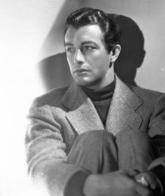 a black and white photo of a man in a suit sitting against a wall with his arms crossed