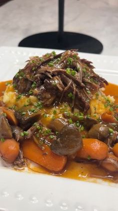 a white plate topped with meat and veggies covered in gravy on top of a table