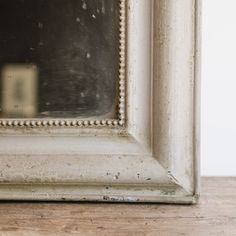 an old white framed mirror sitting on top of a wooden table