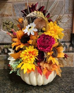 a white pumpkin filled with lots of colorful flowers on top of a granite countertop