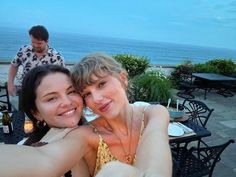 two women taking a selfie at an outdoor restaurant with the ocean in the background