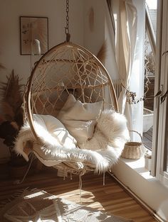 a hanging chair in the corner of a room next to a window with white curtains