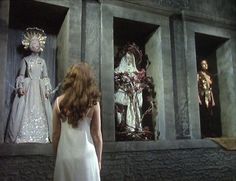 a woman in a white dress standing next to statues