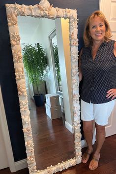 a woman standing in front of a large mirror with shells on the bottom and sides