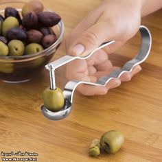 a person is holding an olive slicer in front of some olives on a wooden table