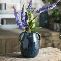 a blue vase filled with purple flowers on top of a wooden table