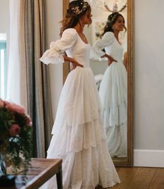 a woman standing in front of a mirror wearing a white wedding dress with ruffles