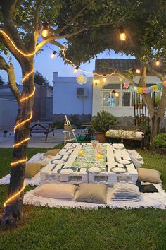 an outdoor dining table is set up in the yard with string lights strung around it