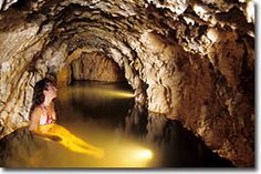 a woman sitting in the middle of a cave next to a body of water with yellow lights