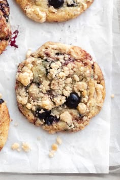 four blueberry crumbled cookies sitting on top of white parchment paper next to each other