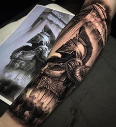 a man's arm with tattoos on it and an image of a statue in the background