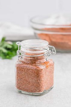 a glass jar filled with spices next to a bowl full of seasoning