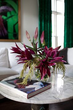 a vase filled with flowers sitting on top of a table next to a book and window