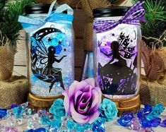 two glass jars with designs on them sitting next to some blue and purple confetti