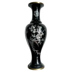 a black vase with white flowers painted on the side and gold trimming around it