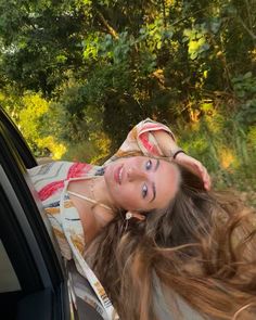 a woman with long hair leaning out the window of a car looking at the camera