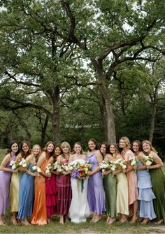 a group of women standing next to each other in front of trees and grass holding bouquets