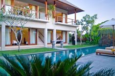 a house with a pool in front of it next to a lush green yard and palm trees