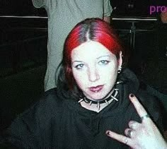 a woman with red hair and piercings pointing at the camera while standing next to a man